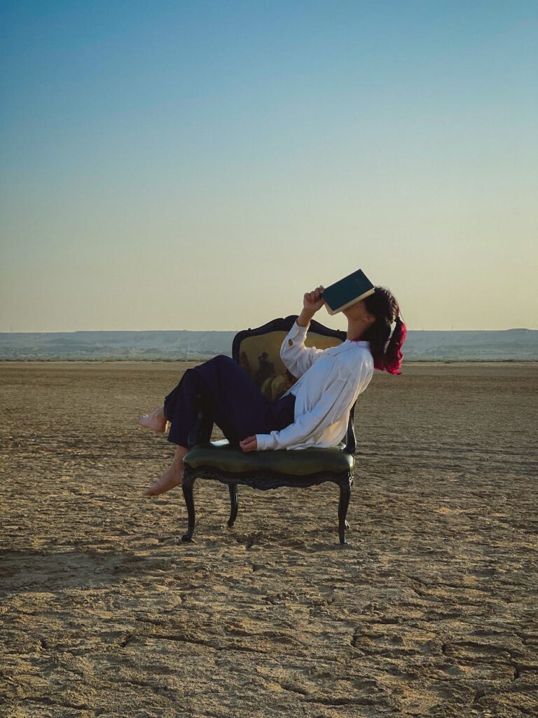 woman with a book on a wide old fashioned chair in the desert