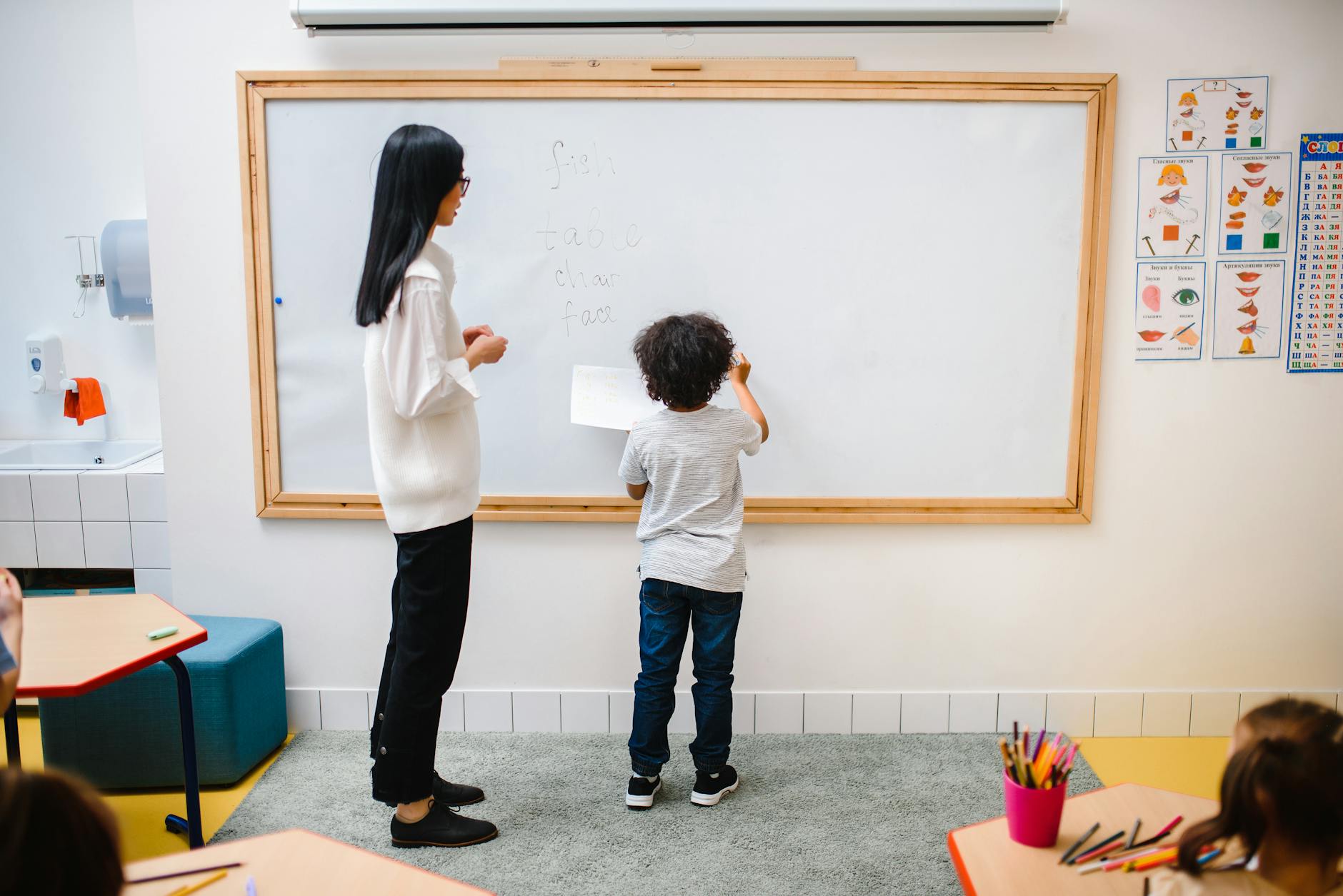 woman and a boy standing by a whiteboard in a classroom